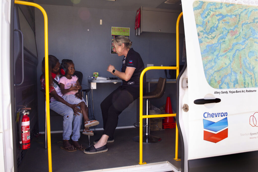 Mother and child sitting in the mobile bus with an audiologist.