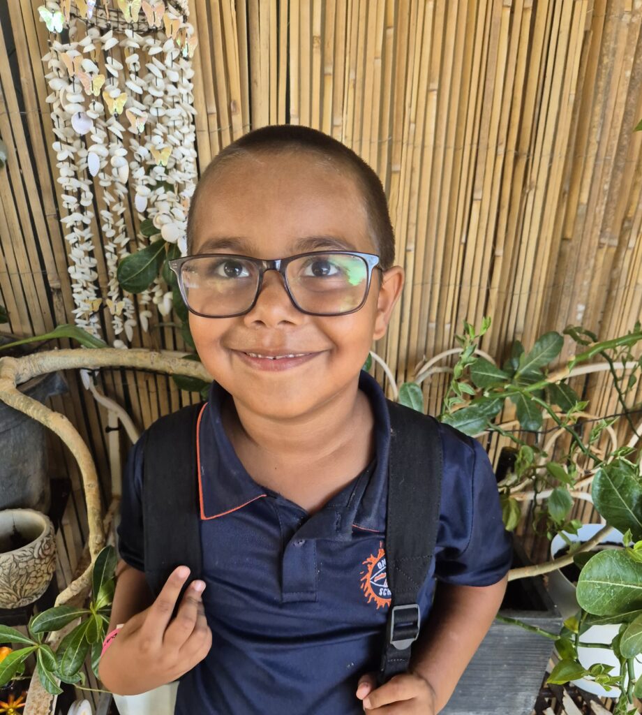 Young child smiling to camera wearing glasses.